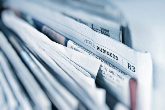 A close-up of a stack of newspapers, with the headline World Business visible, suggesting global business news—perhaps even features on innovations like golf simulators or trends in golf sim technology. The edges of the papers are slightly rumpled.